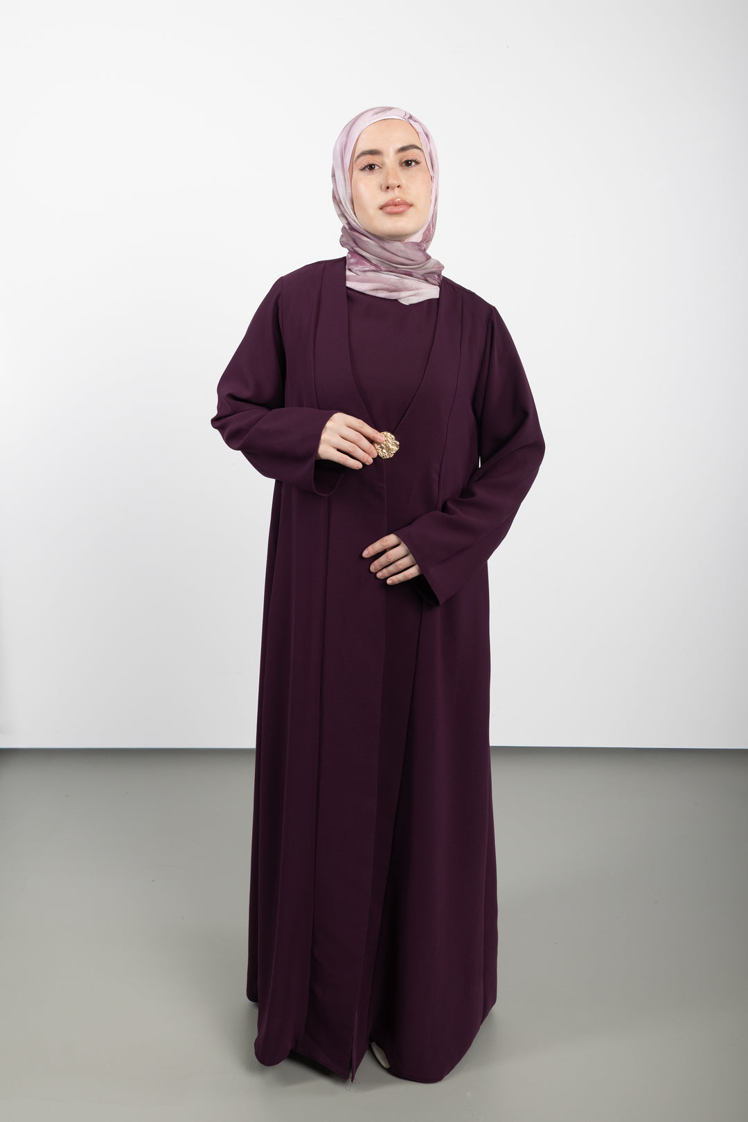 Woman wearing a long burgundy dress and hijab on a white background