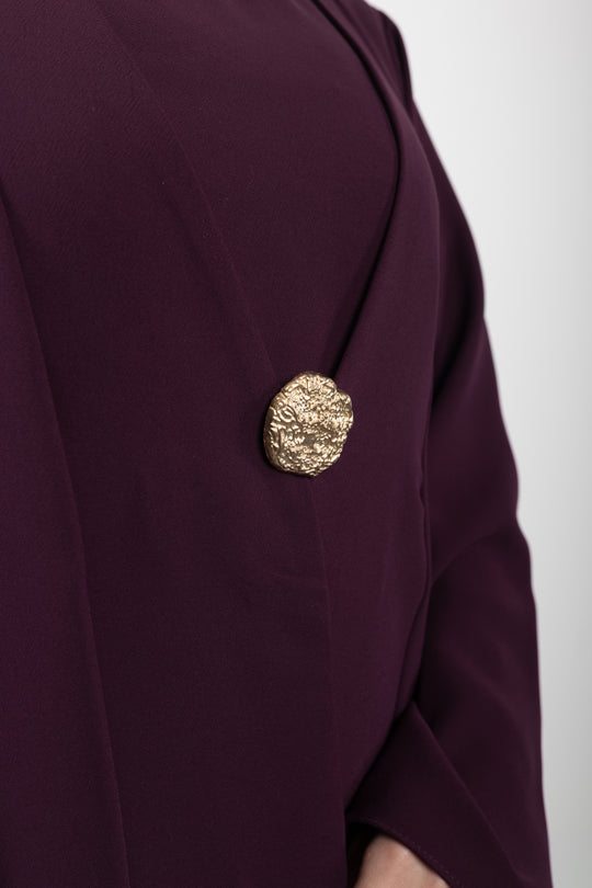 Close-up of a burgundy blazer with a gold button on a white background