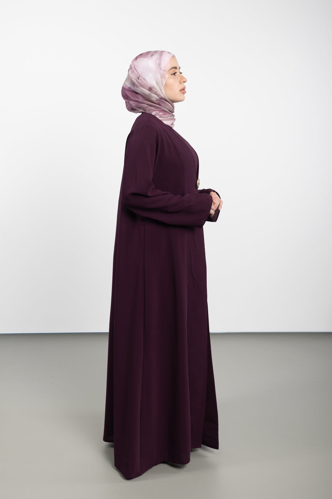 Woman wearing a long dark purple dress and a pink hijab on a white background