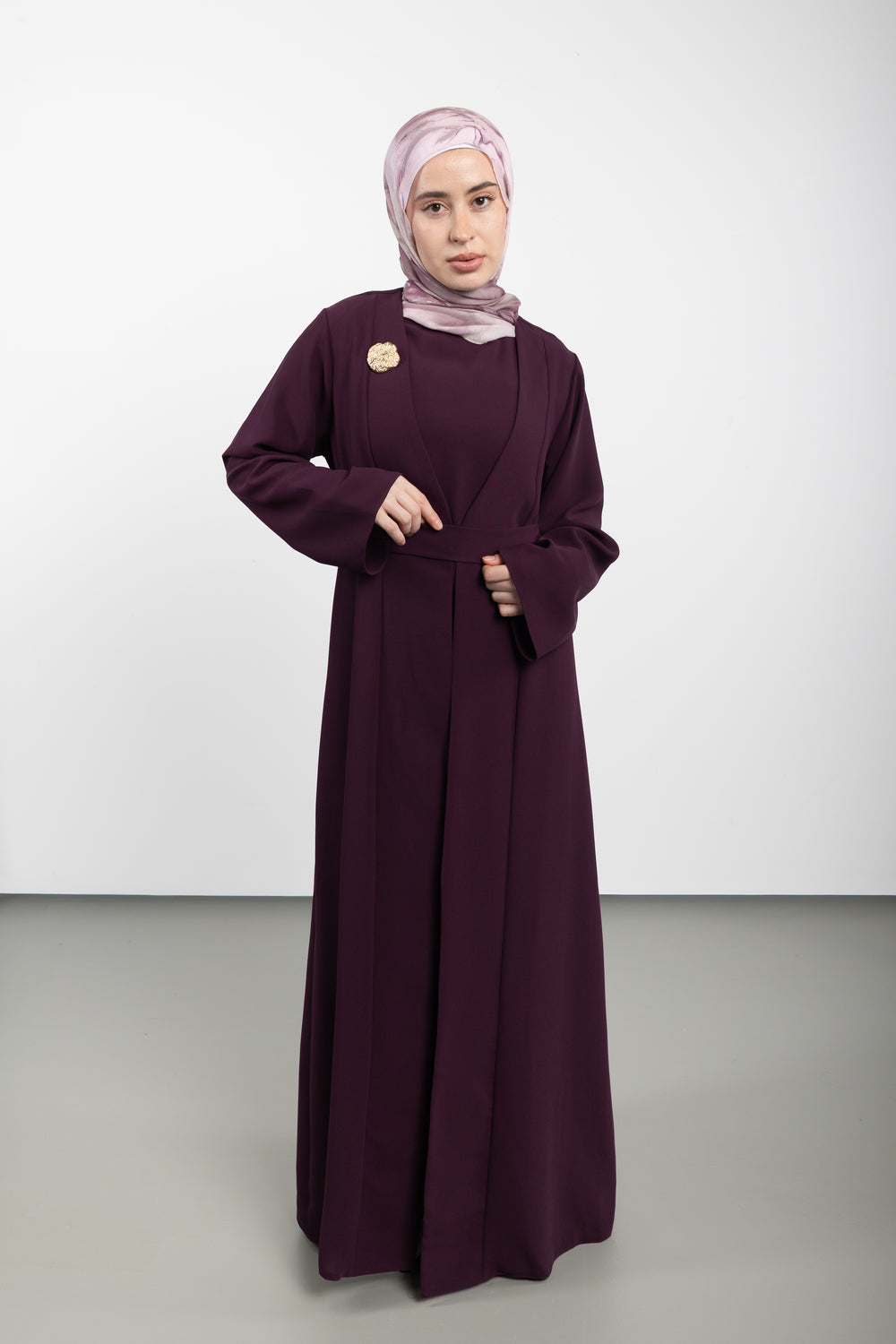 Woman wearing a long dark purple dress with a matching hijab on a white background