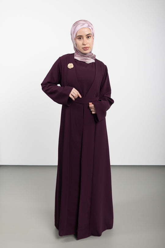 Woman wearing a long dark purple dress with a matching hijab on a white background