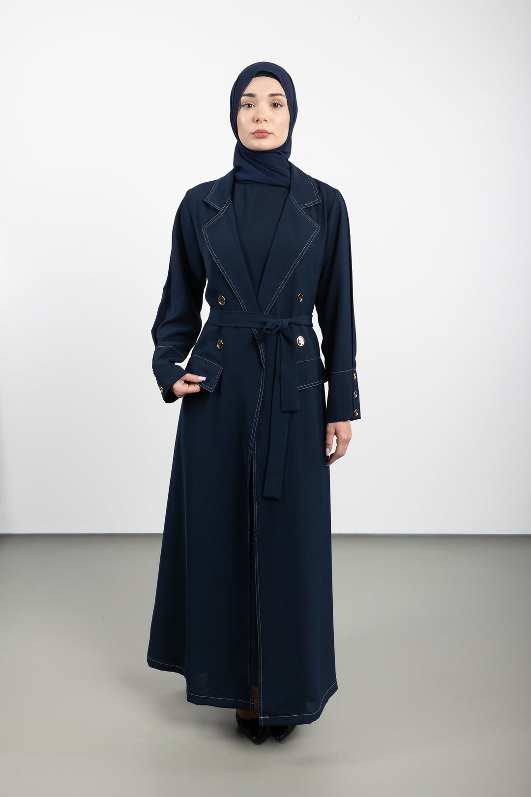 Woman wearing a long navy coat and hijab on a white background
