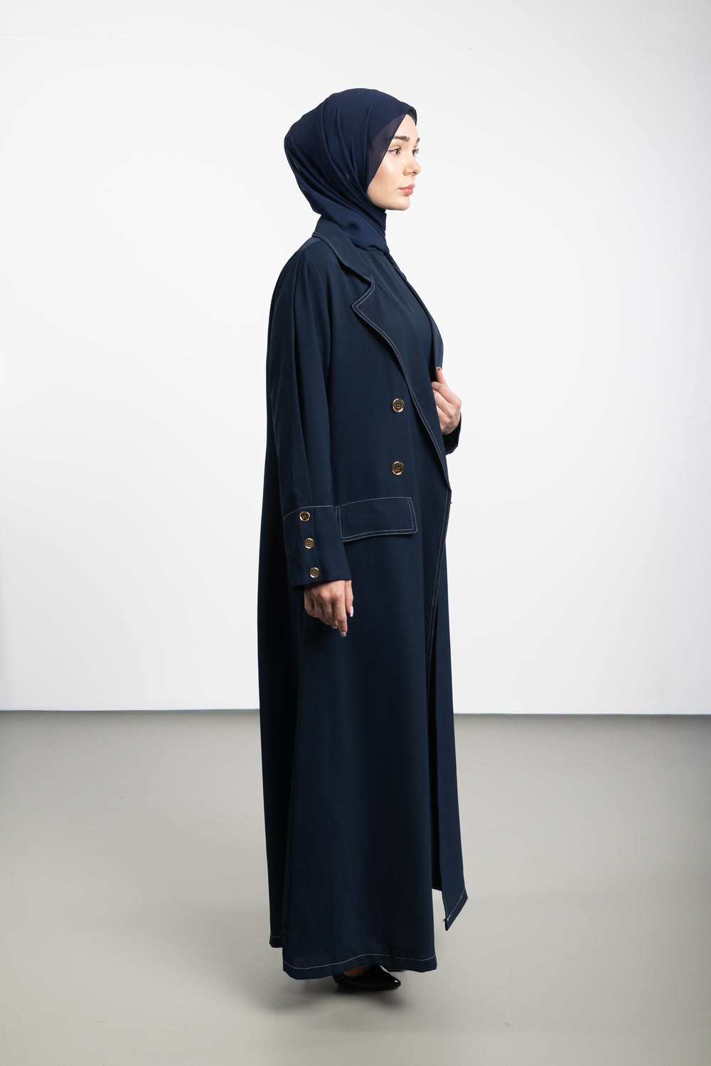 Woman wearing a long navy coat and hijab on a white background