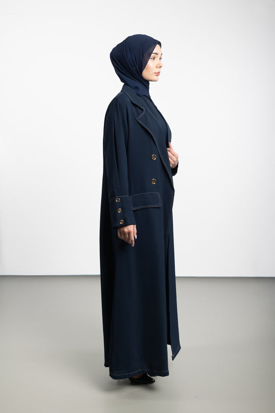 Woman wearing a long navy coat and hijab on a white background