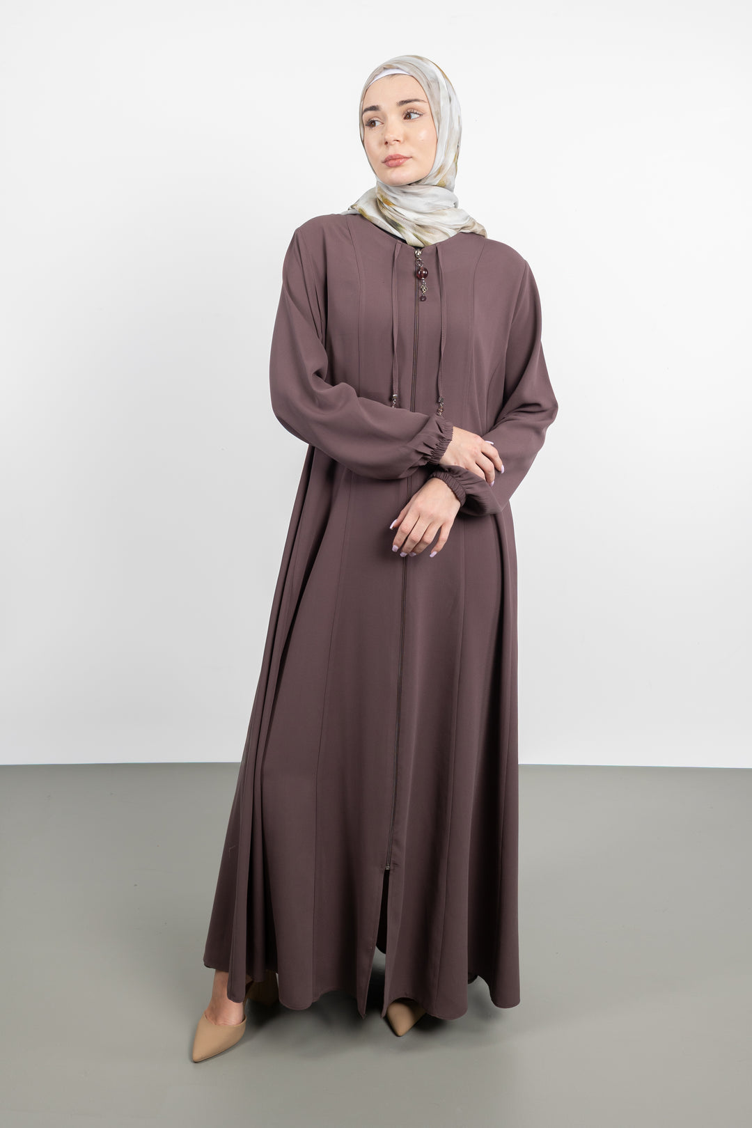 Woman wearing a long brown dress and hijab on a white background