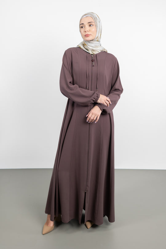 Woman wearing a long brown dress and hijab on a white background