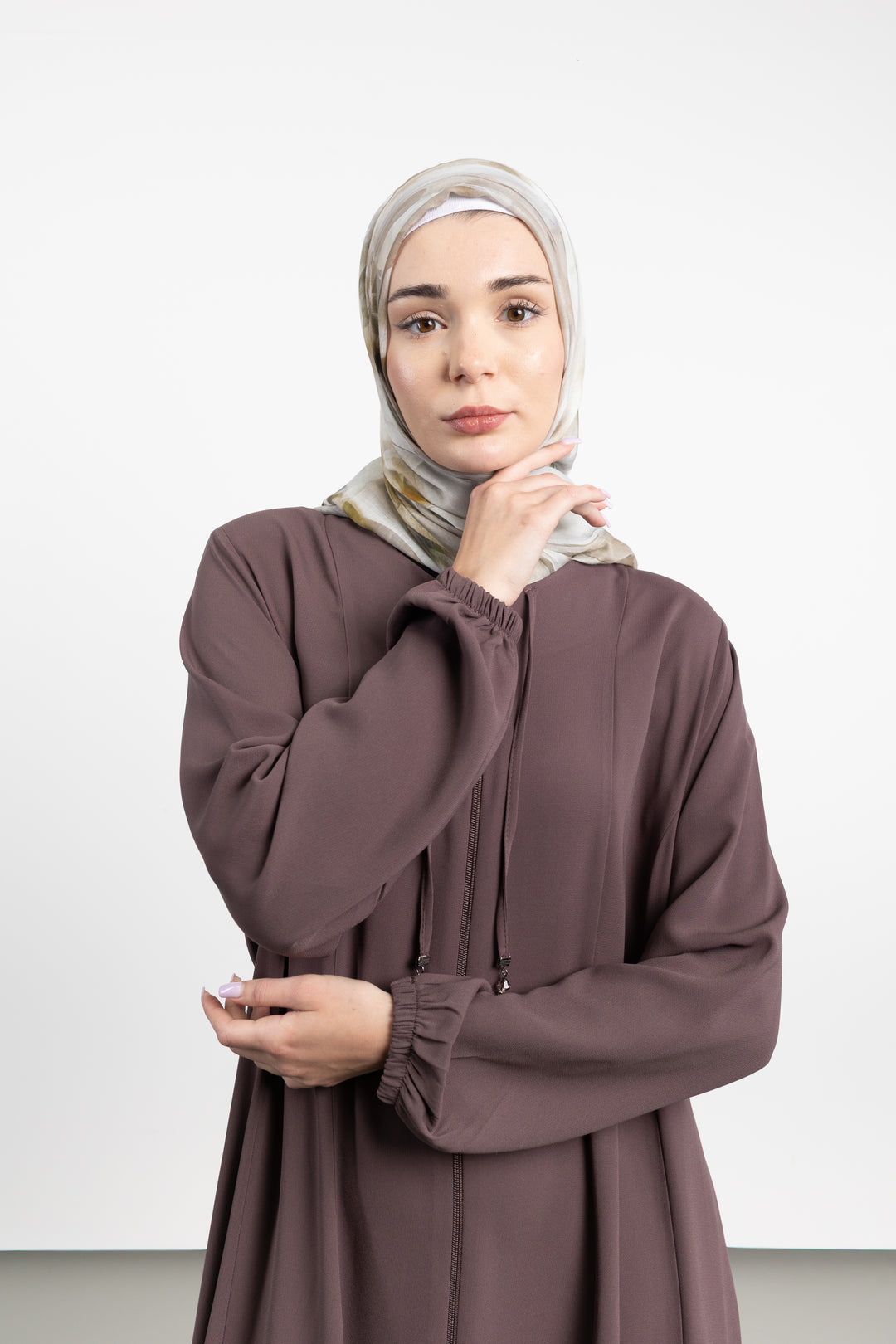 Woman wearing a brown dress and hijab against a white background