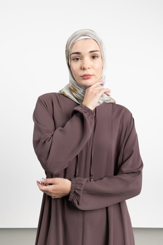 Woman wearing a brown dress and hijab against a white background