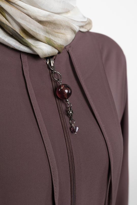 Close-up of a brown jacket with a zipper and decorative pendant, featuring a scarf in the background.