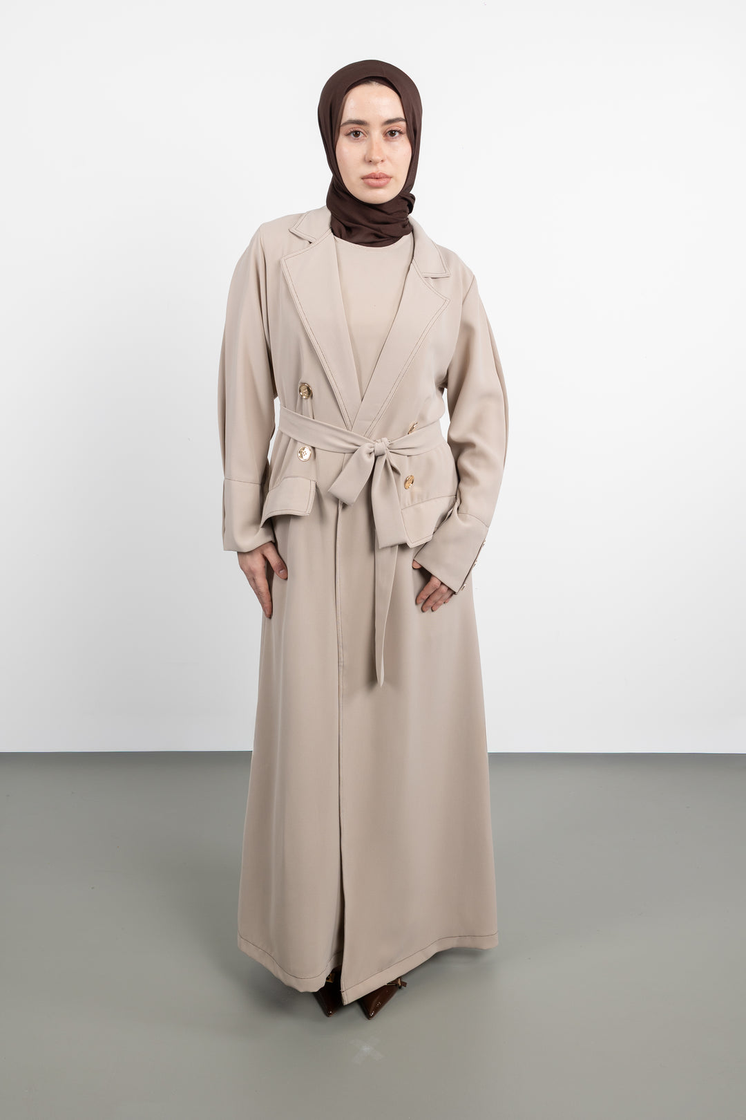 Woman wearing a long beige coat with a belt on a white background