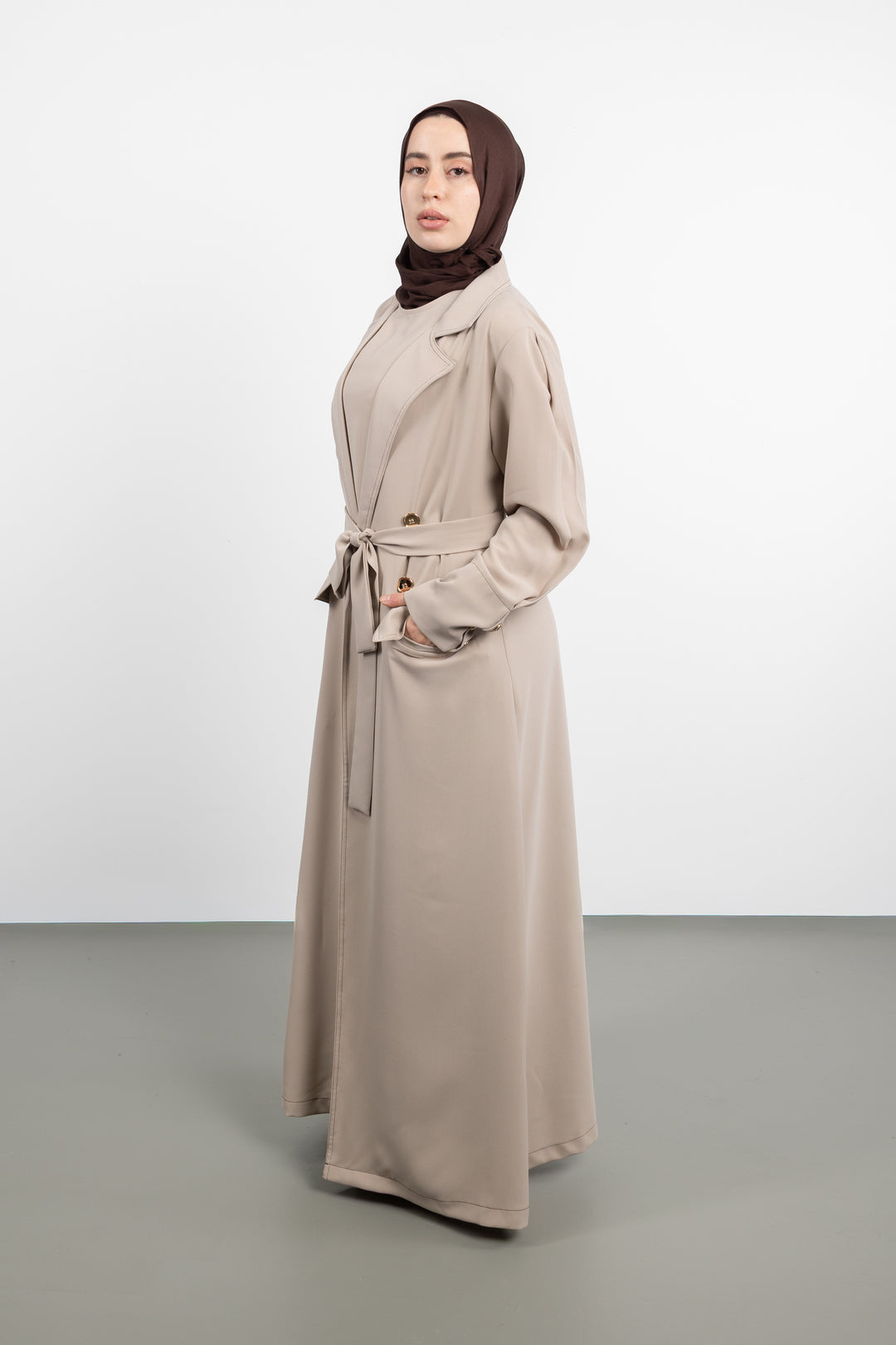 Woman wearing a long beige coat and hijab on a white background