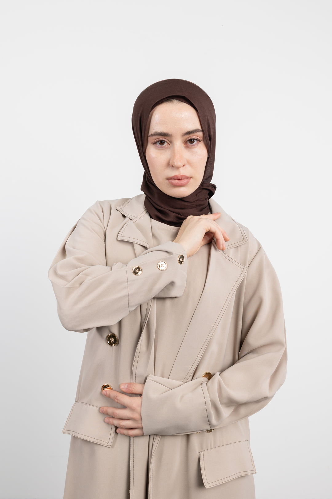 Woman wearing a beige Abaya and brown hijab on a white background