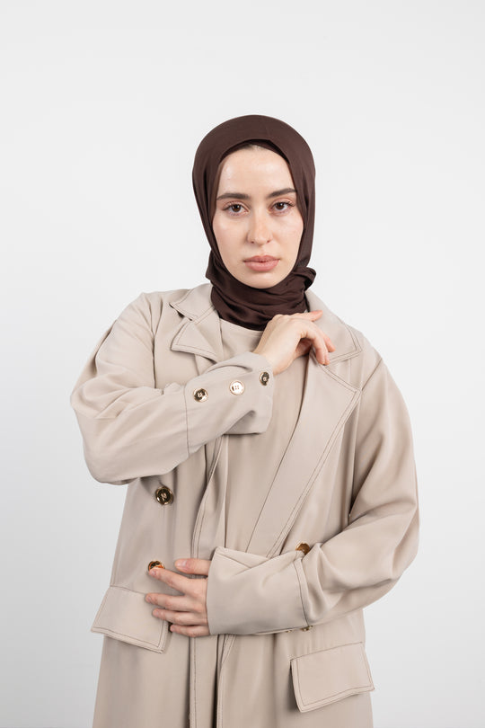 Woman wearing a beige Abaya and brown hijab on a white background