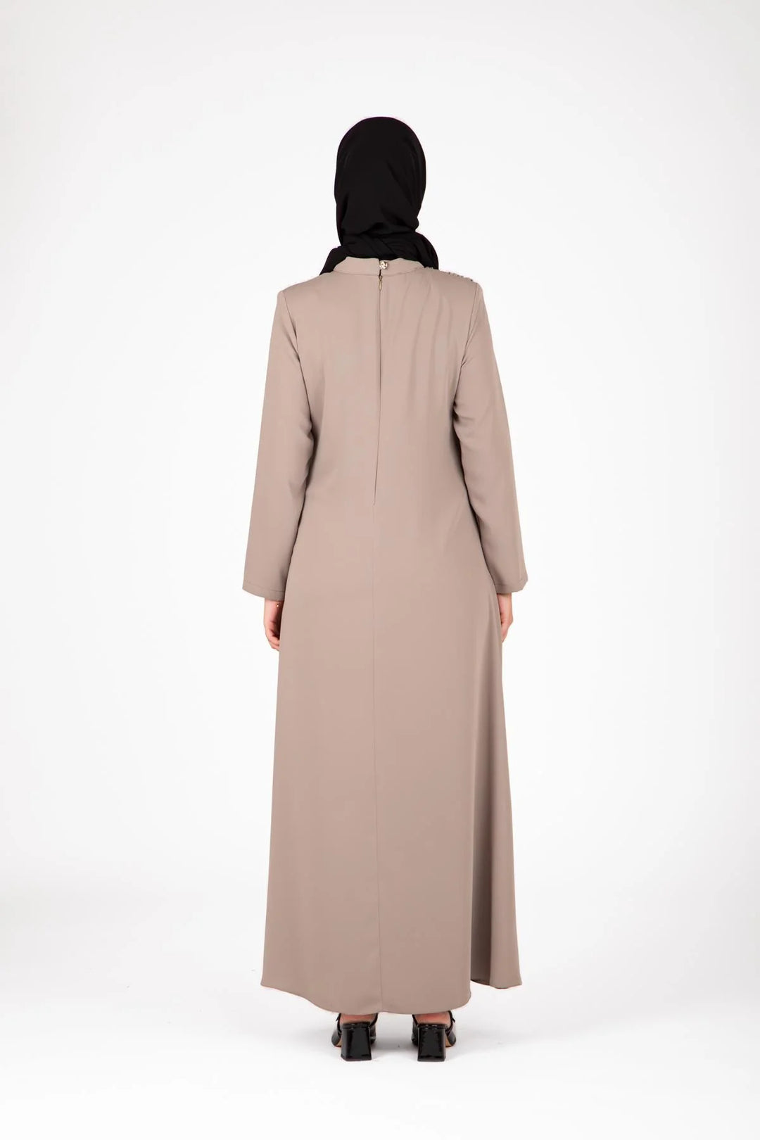 Person wearing a beige abaya and black hijab on a white background